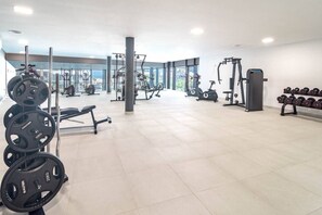 Un gimnasio con equipo de levantamiento de pesas, máquinas de cardio y mancuernas.