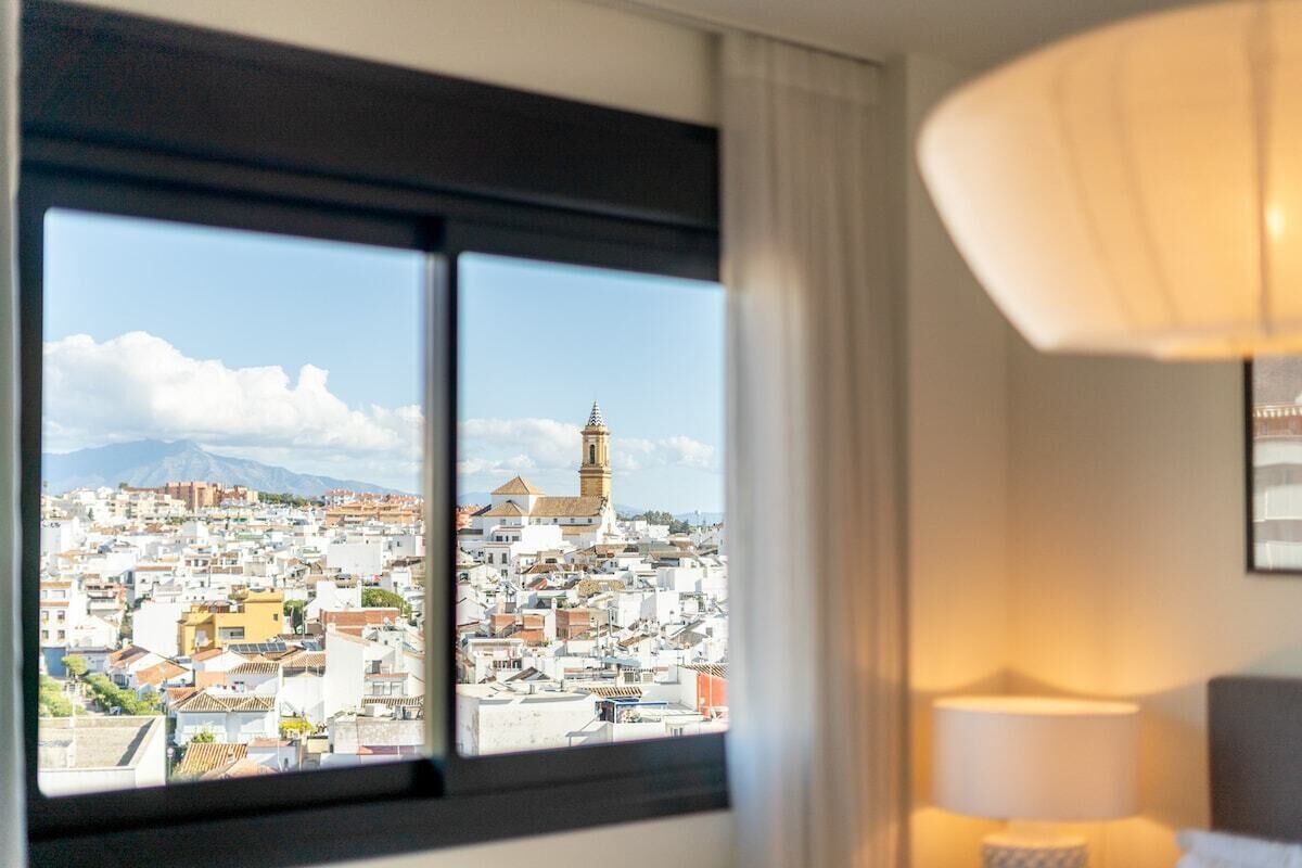 A hotel room with a large window offering a view of a cityscape, including a prominent tower.