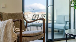 A cozy seating area with a cushioned chair and a small table, a balcony with chairs, and a view of the cityscape. - Inf26f - Modern and Bright City Apartment (Estepona)