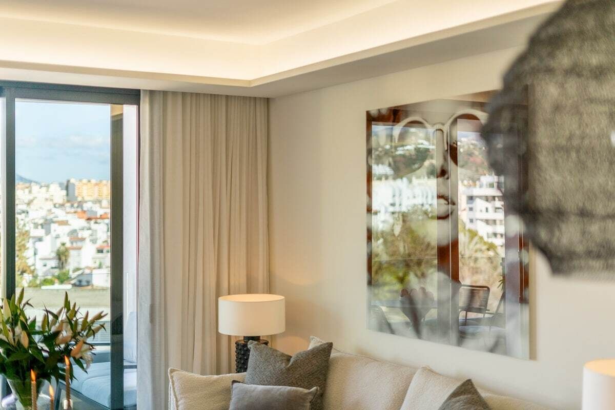 A modern living room with a large window, a sofa, a lamp, and a decorative wall piece.