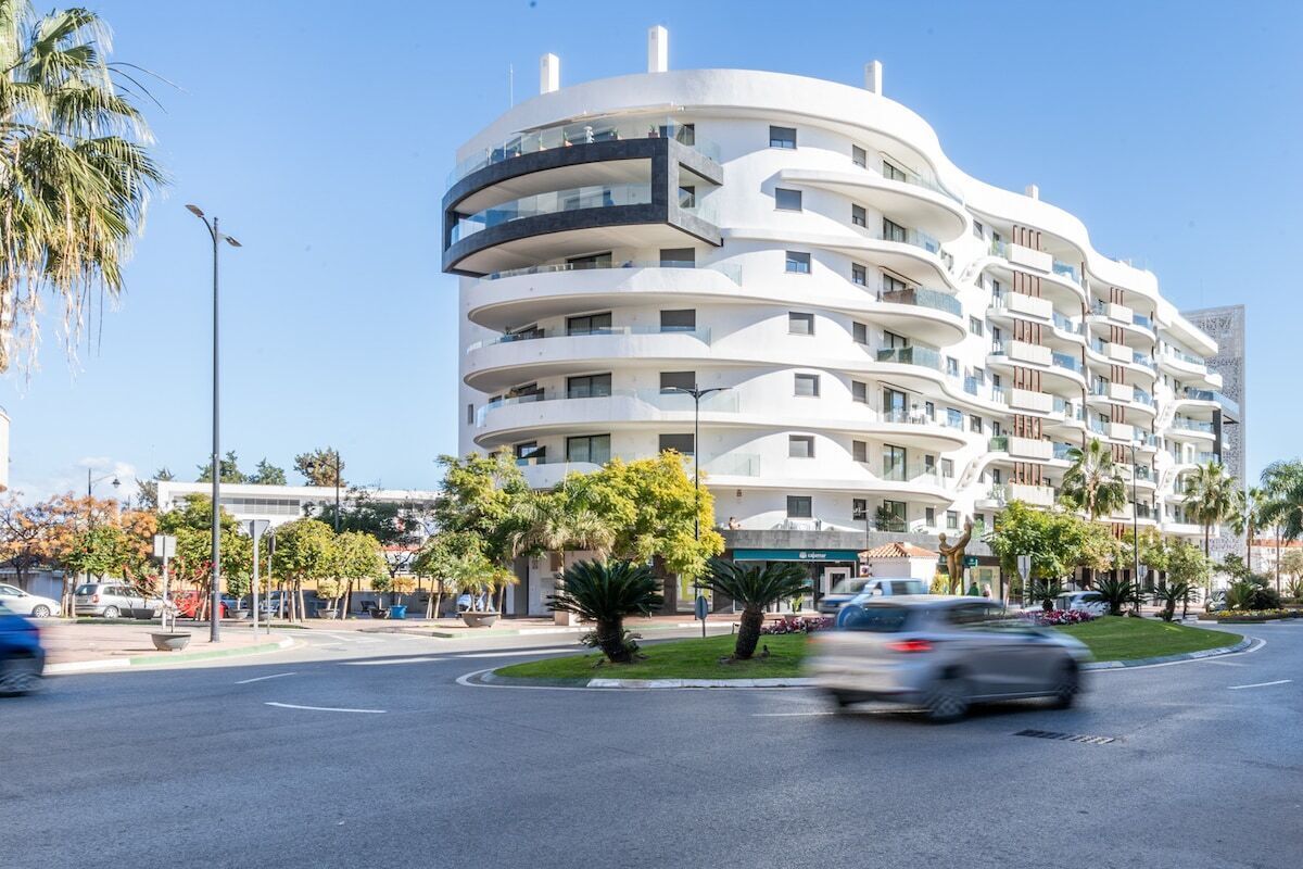 A multi-story hotel with a curved facade, balconies, and a landscaped area with palm trees.