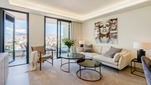 A modern living room with a sofa, two armchairs, a coffee table, and a view of the city through large windows. - Inf26f - Modern and Bright City Apartment (Estepona)