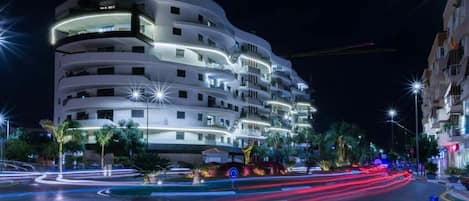 Et hotel med flere etager, altaner, en buet facade og oplyste vinduer.