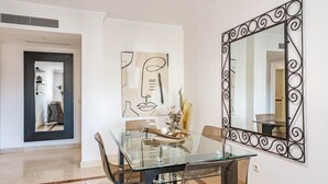 Un comedor con una mesa y sillas de vidrio, un espejo grande con marco decorativo y arte abstracto en la pared.