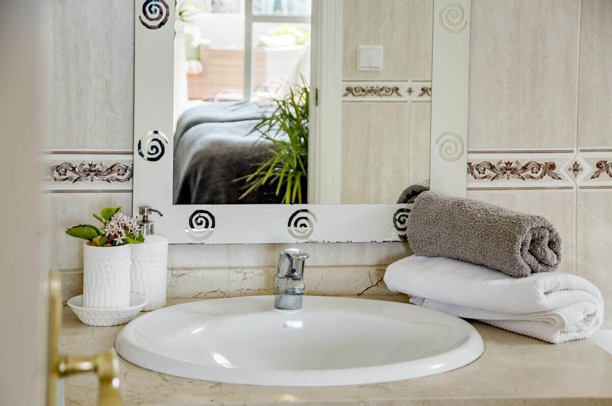Un baño con un lavamanos blanco, un espejo con adornos en espiral, una toalla y una planta en maceta.