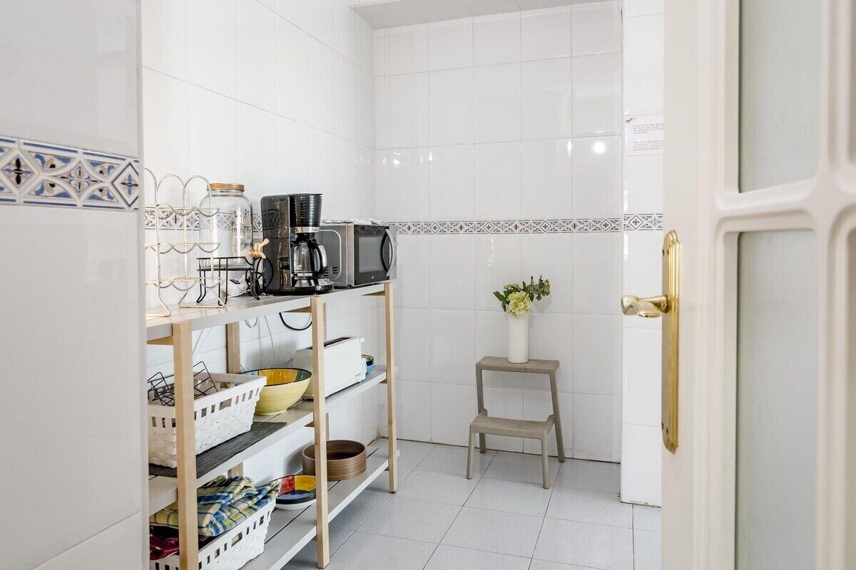 A kitchen with white tiled walls, a coffee maker, a microwave, and shelves with baskets and containers.