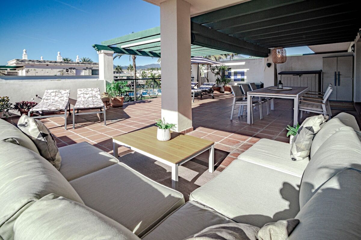 A rooftop patio with outdoor seating, a table, and a pergola.