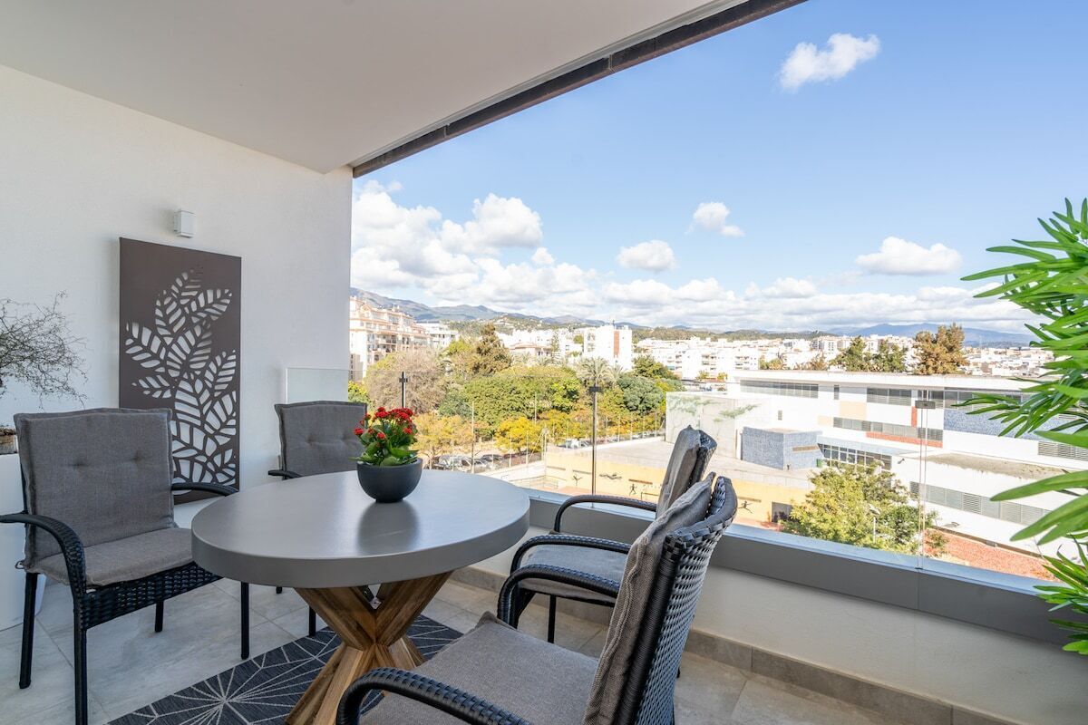A balcony with a round table, chairs, and a potted plant.