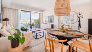 Un salon moderne avec une table à manger ronde, un luminaire suspendu en osier et une grande fenêtre donnant sur la ville.