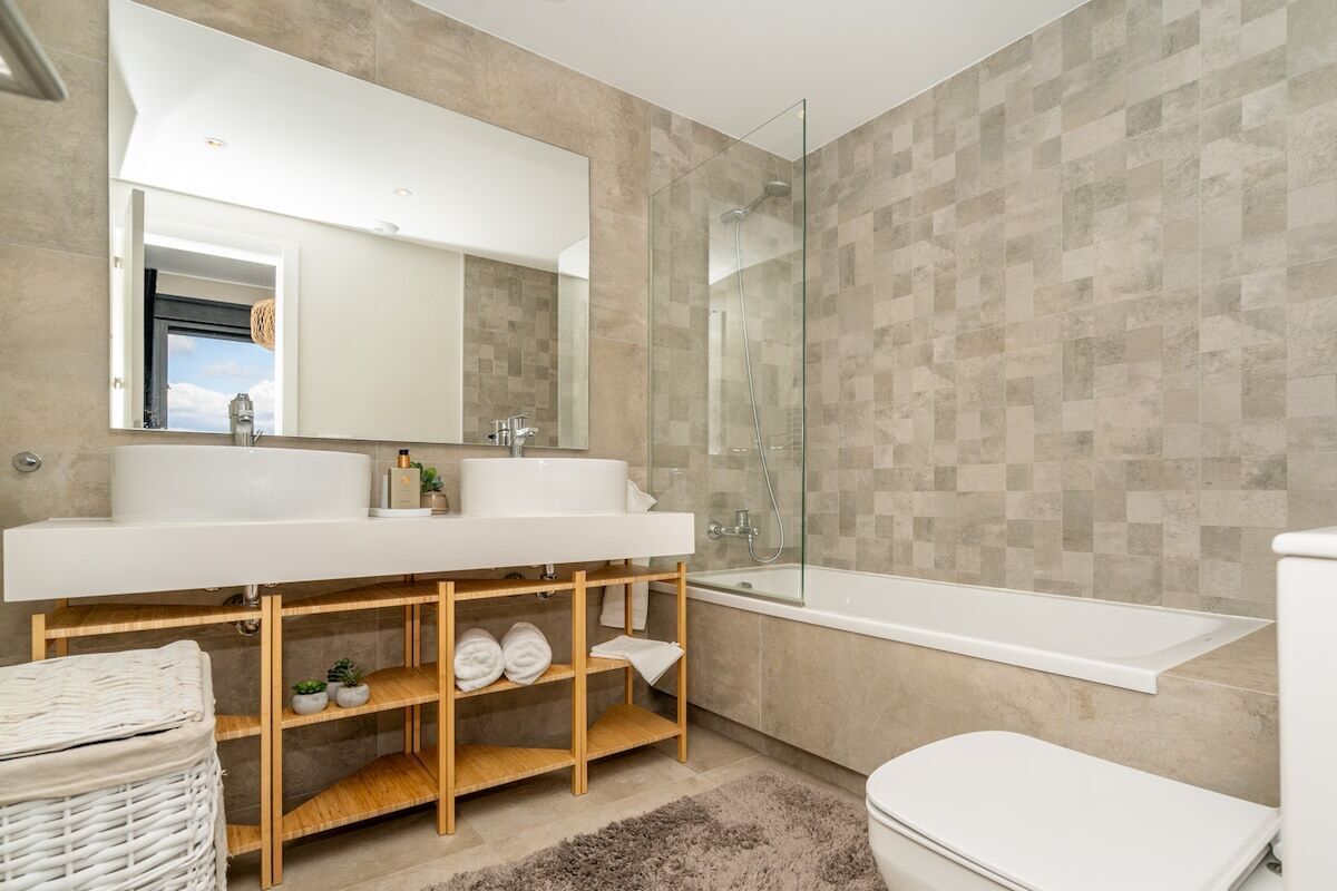 A modern bathroom with a large mirror, two sinks, a glass shower enclosure, and a bathtub.