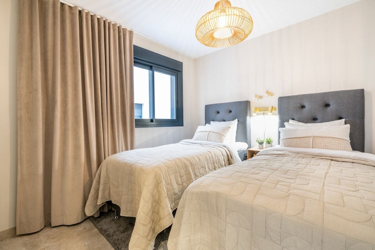 Ein Hotelzimmer mit zwei Betten, einem großen Fenster, einer Pendelleuchte und Blick ins Freie.