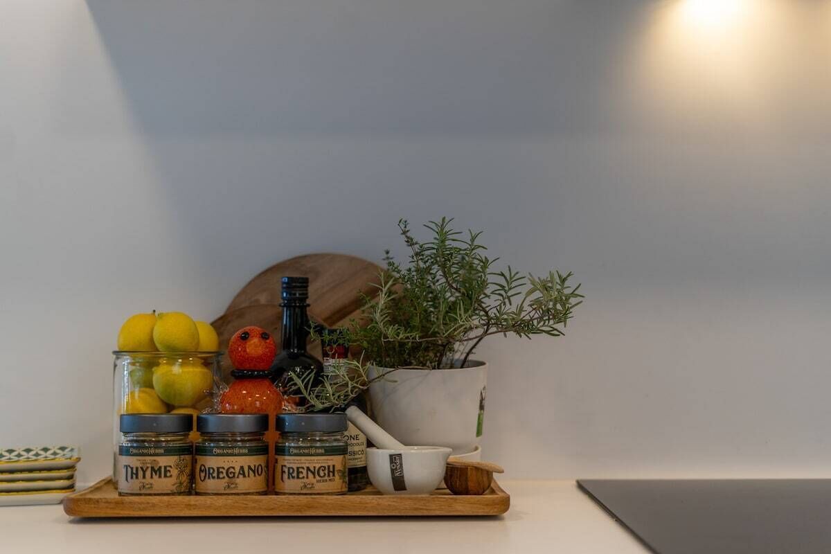 Un plan de travail de cuisine avec des bocaux étiquetés « Thym », « Origan » et « Herbes de Provence », une bouteille, une plante en pot et une cuillère en bois.