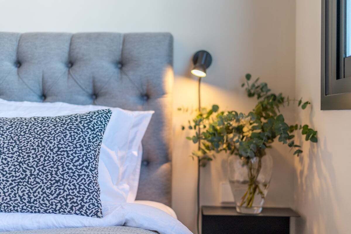 A bedroom with a tufted headboard, a bedside table with a lamp, and a potted plant.