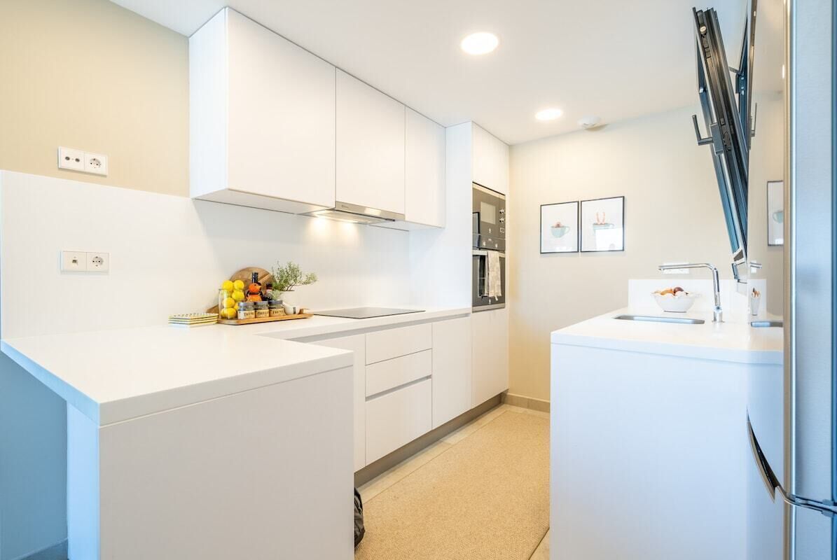 A modern kitchen with white cabinetry, a stainless steel refrigerator, and a built-in oven.