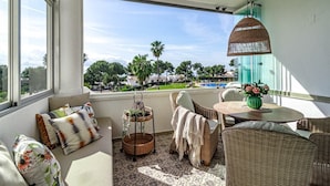A balcony with wicker furniture, a wicker hanging light fixture, and a view of a swimming pool and greenery. - Jm94 - Totally Renovated in Stylish Design (Mijas)