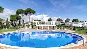 A swimming pool with a tiled deck, surrounded by greenery and white buildings. - Jm94 - Totally Renovated in Stylish Design (Mijas)