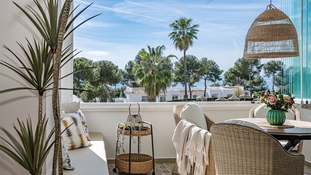 A balcony with wicker furniture, a woven basket, and a view of palm trees and buildings. - Jm94 - Totally Renovated in Stylish Design (Mijas)