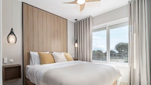 A modern bedroom with a large bed, a ceiling fan, a nightstand, a wall-mounted lamp, and a window with curtains. - Jm94 - Totally Renovated in Stylish Design (Mijas)