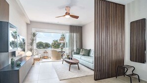 A modern living room with a sofa, coffee table, and a TV on a black console. There is a large window with curtains, a ceiling fan, and a view of palm trees outside. - Jm94 - Totally Renovated in Stylish Design (Mijas)