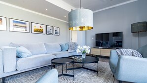 Ein modernes Wohnzimmer mit einer Eckcouch, einem Couchtisch, einem Fernseher und einem gemusterten Teppich.