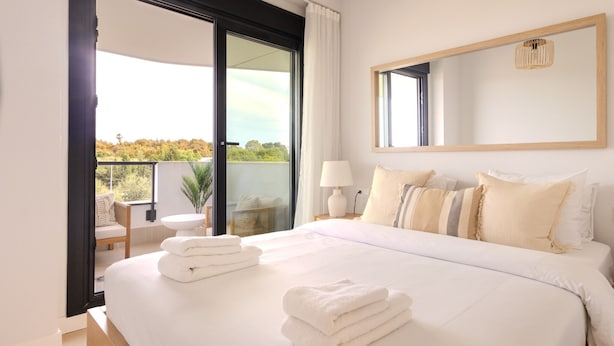 A hotel room with a large bed, a balcony, a chair, a table, and a mirror. - Ae22b - New Build w/ Pool, gym & Sunny Balcony (Estepona)