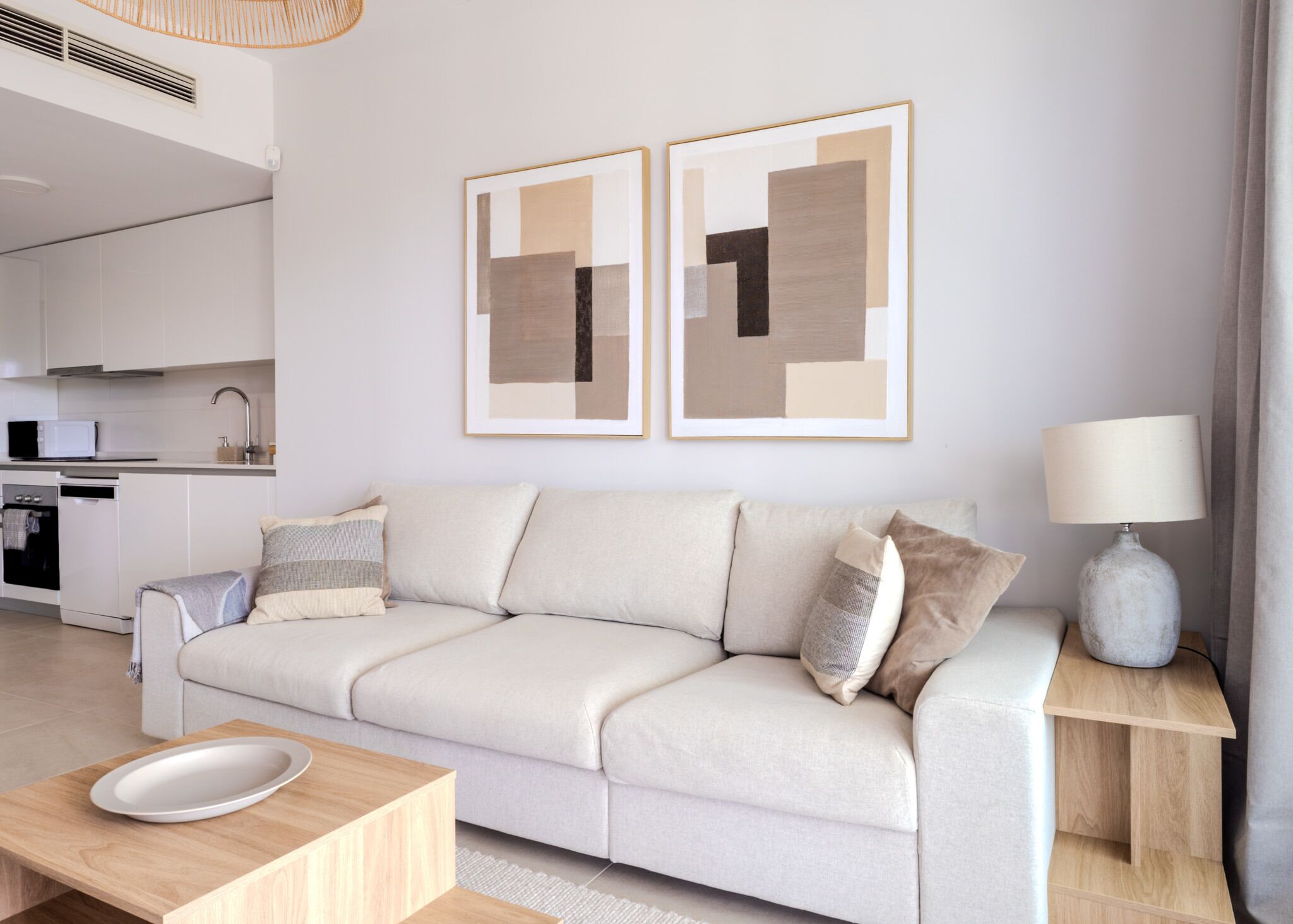 Un salon moderne avec un canapé, une table basse, une table d’appoint avec une lampe, et un coin cuisine à l’arrière-plan.