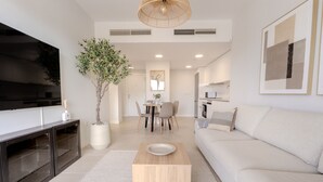 A modern living room with a flat-screen TV, a dining area with chairs, a sofa, and a potted plant. - Ae22b - New Build w/ Pool, gym & Sunny Balcony (Estepona)