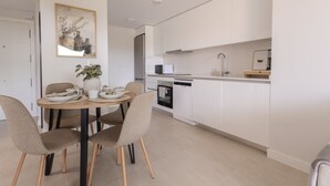 A modern kitchen with white cabinets, a dining table with chairs, and a small island with a plant. - Ae22b - New Build w/ Pool, gym & Sunny Balcony (Estepona)