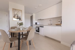 Une cuisine moderne avec des meubles blancs, une table à manger avec des chaises et un petit îlot central agrémenté d’une plante.