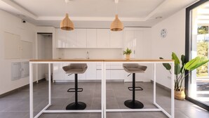 A modern kitchen with white cabinets, a wooden countertop, two bar stools, and pendant lights. - Ae22b - New Build w/ Pool, gym & Sunny Balcony (Estepona)