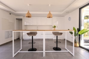 Une cuisine moderne avec des armoires blanches, un comptoir en bois, deux tabourets de bar et des luminaires suspendus.
