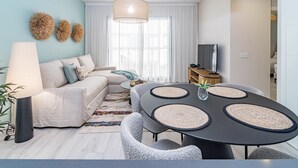 Un salon moderne avec un canapé, une table à manger avec des sets de table, une lampe et un téléviseur.