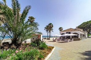 Un bâtiment situé sur la côte, doté d’une terrasse, de palmiers et offrant une vue sur la mer.