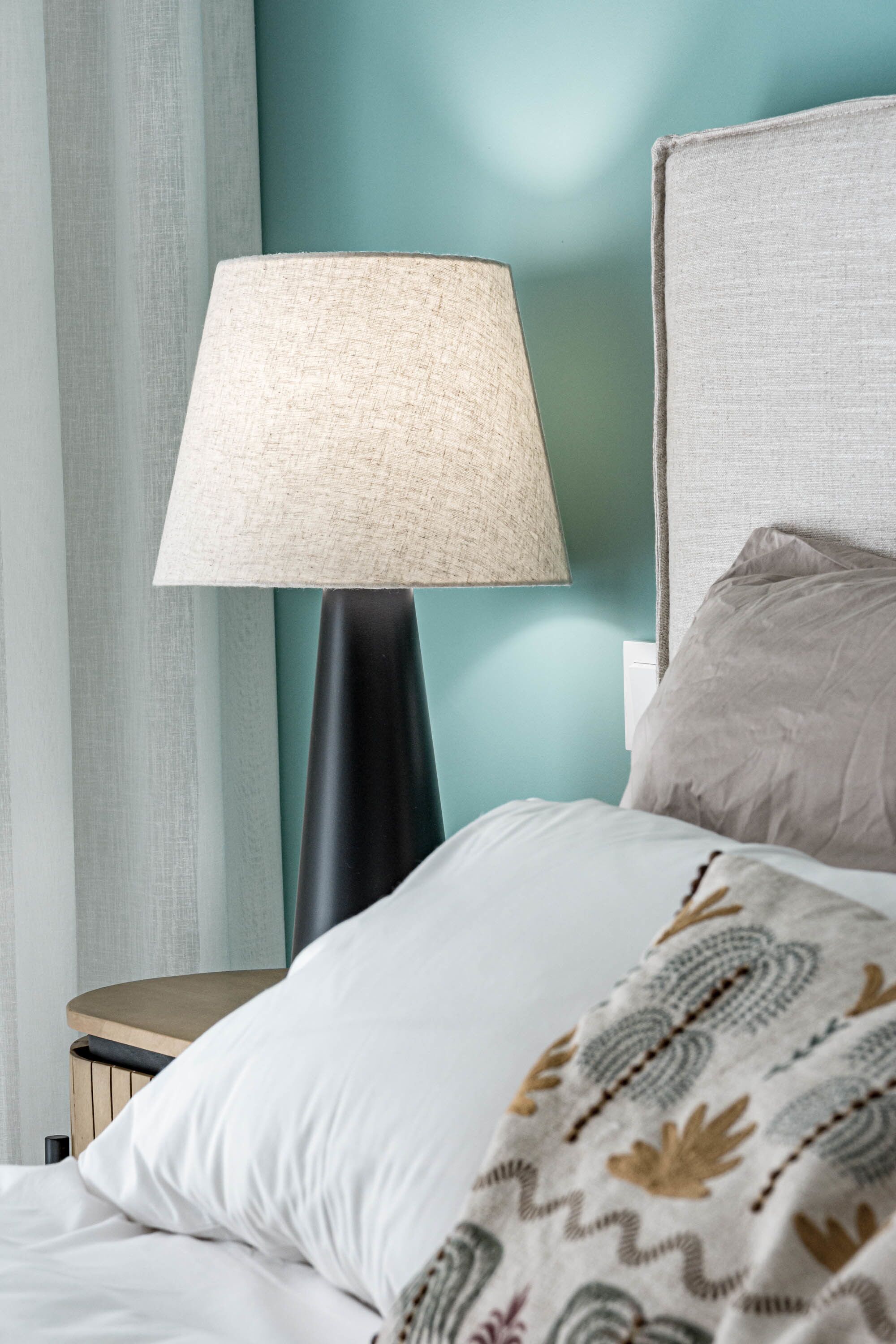 A bed with a patterned throw, a lamp, and a nightstand.