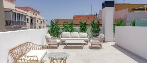 A rooftop terrace with a sofa set, wicker chairs, and a glass table.