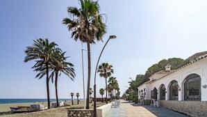 Une promenade en bord de mer bordée de palmiers, une plage et un bâtiment doté d’arcades.