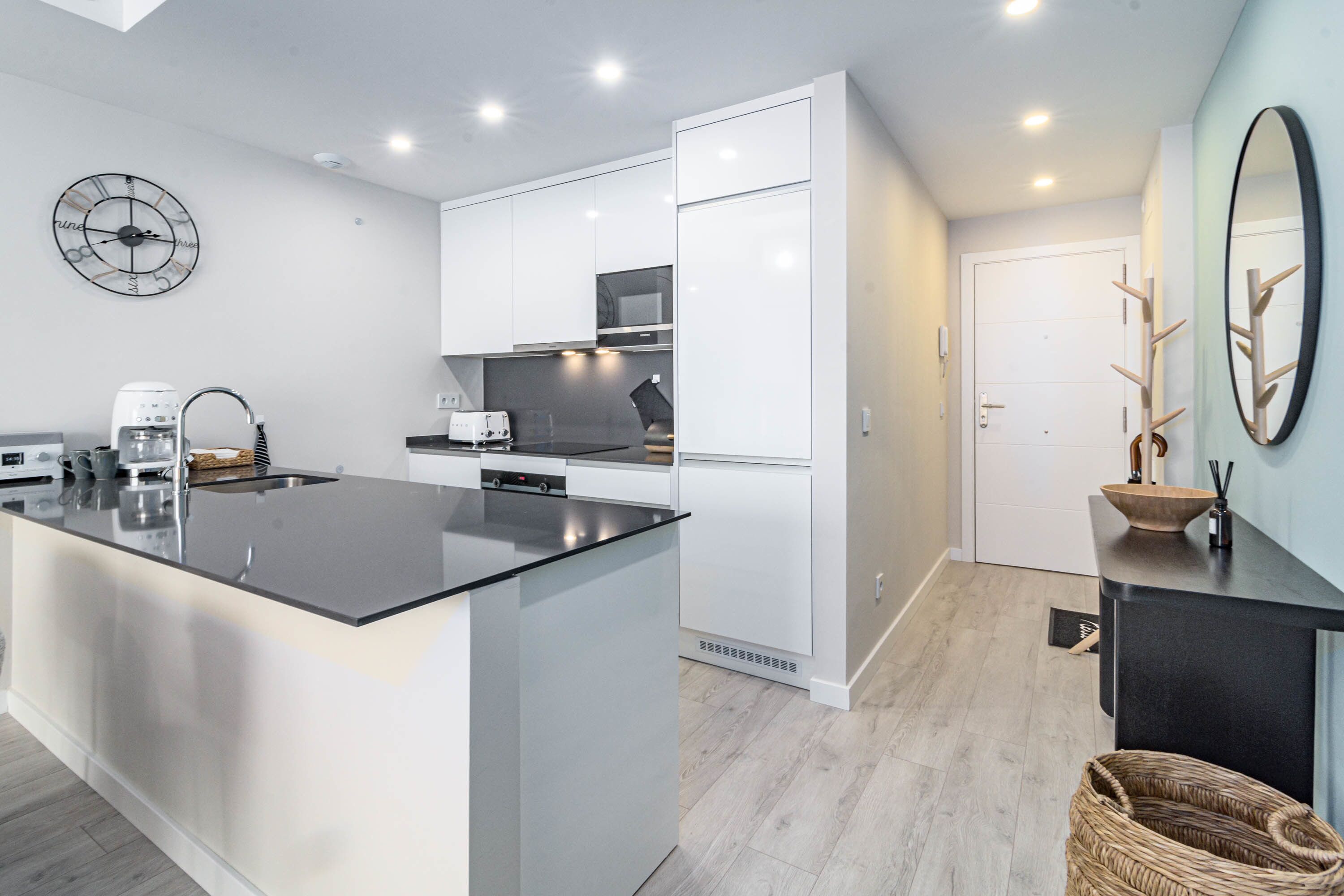 A modern kitchen with white cabinetry, a central island, and a clock on the wall.