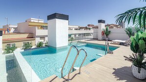 Une piscine sur le toit, avec une eau d’un bleu limpide, des échelles métalliques et des plantes en pot.
