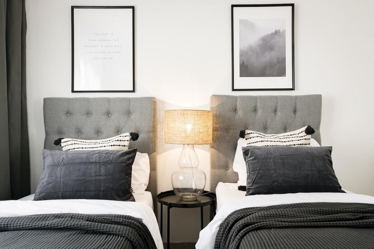 A hotel room with two beds, a nightstand with a lamp, and two framed pictures on the wall.