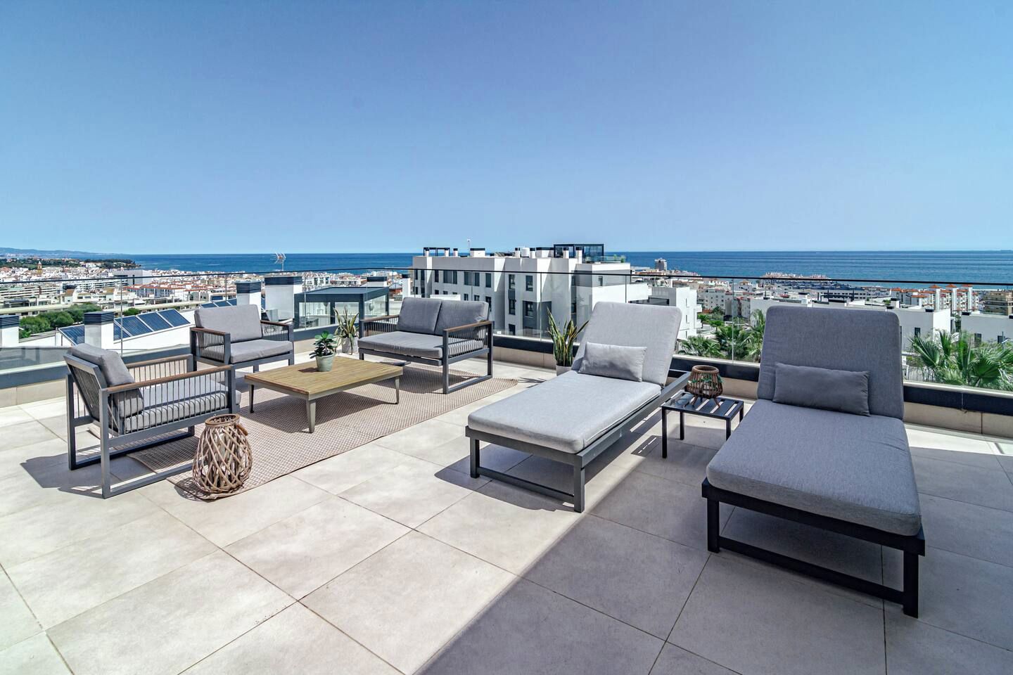 Une terrasse sur le toit, aménagée avec du mobilier d’extérieur, offrant une vue sur la mer et sur les bâtiments qui se dressent à l’arrière-plan.