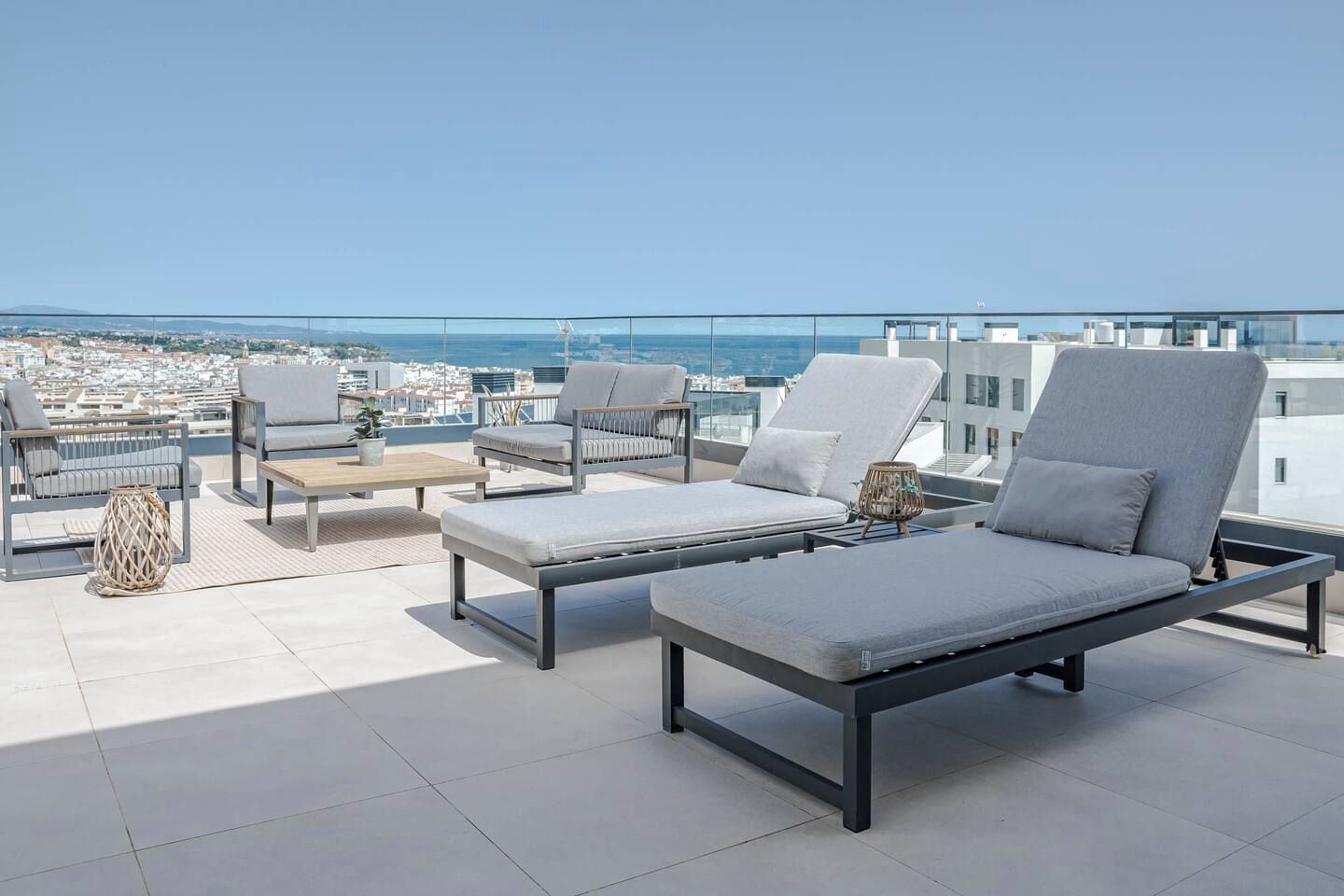 A rooftop terrace with lounge chairs, a table, and a view of the city and sea.