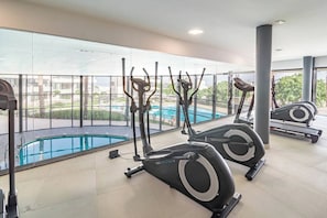 A gym with stationary bikes and a pool visible through large windows. - Lme103a - Bright Modern Flat With Amazing Terrace (Estepona)