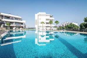 A swimming pool with clear blue water, surrounded by modern buildings and palm trees. - Lme103a - Bright Modern Flat With Amazing Terrace (Estepona)