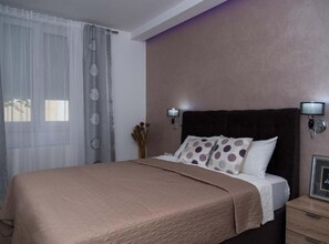 A hotel room with a large bed, a nightstand, two wall-mounted lamps, and a window with sheer curtains.