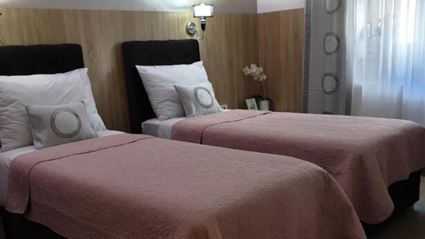 Une chambre d’hôtel avec deux lits, chacun doté d’une tête de lit noire et de draps blancs. On y trouve une petite table sur laquelle est posé un vase de fleurs, ainsi qu’une lampe fixée au mur.