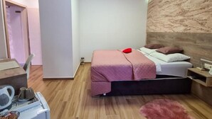 Une chambre moderne avec un lit, une table de chevet et un petit bureau équipé d’une bouilloire et de tasses.