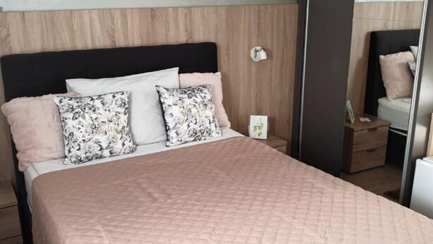 A neatly made bed with a quilted pink bedspread, two floral pillows, and a wooden headboard. - Ginko Rooms - Double Room With Private Bathroom (A1) (Daruvar)