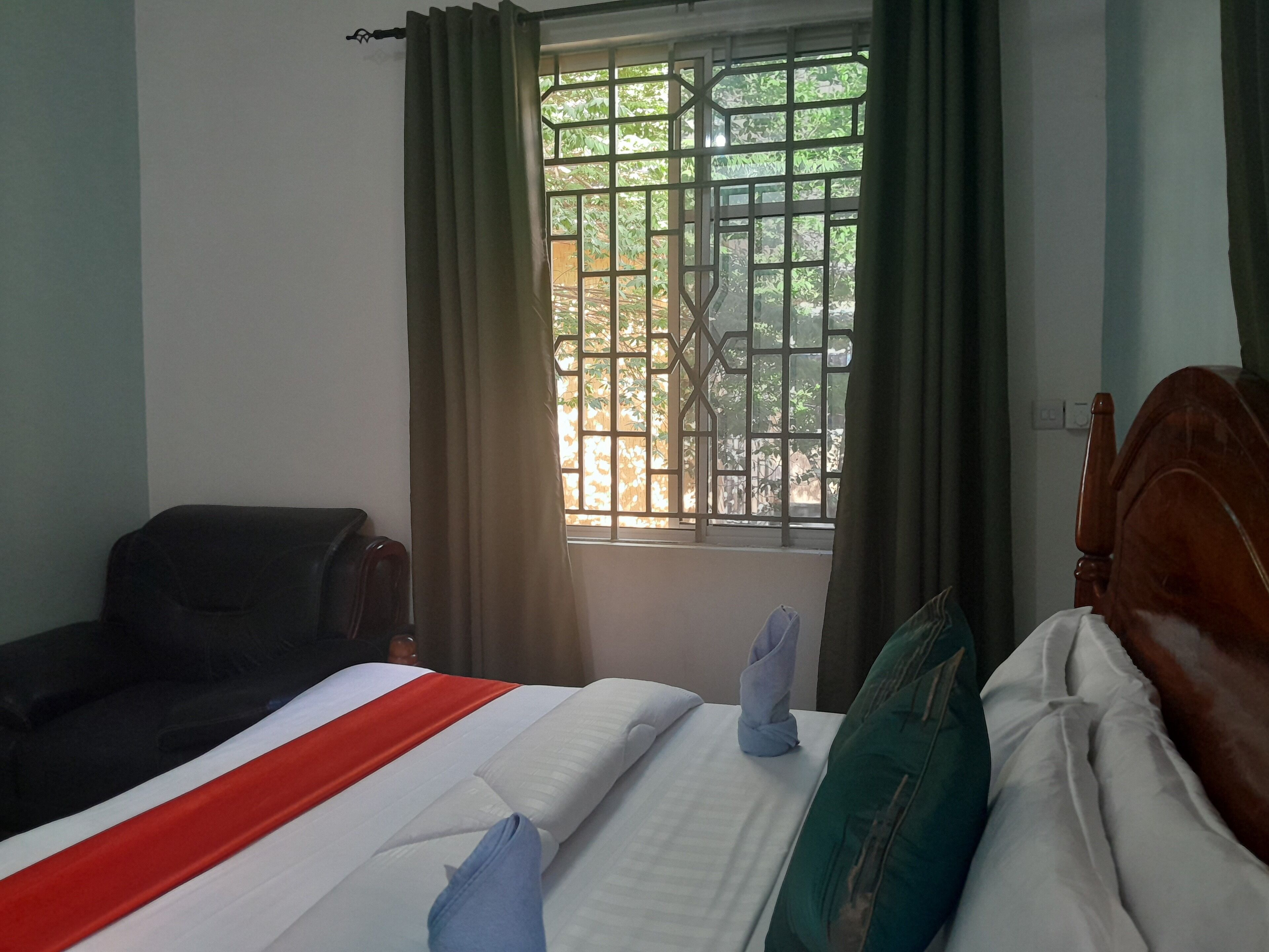 A hotel room with a bed, a chair, a window with a metal grid, and curtains.