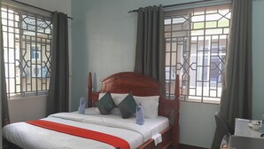 A neatly made bed with a wooden headboard, white and red bedding, and a view of the outside through barred windows. - DAG HOTEL MOROGORO (Morogoro)