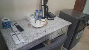 A kitchenette with a coffee maker, two bottles of water, a remote control, a roll of toilet paper, and a small refrigerator. - DAG HOTEL MOROGORO (Morogoro)